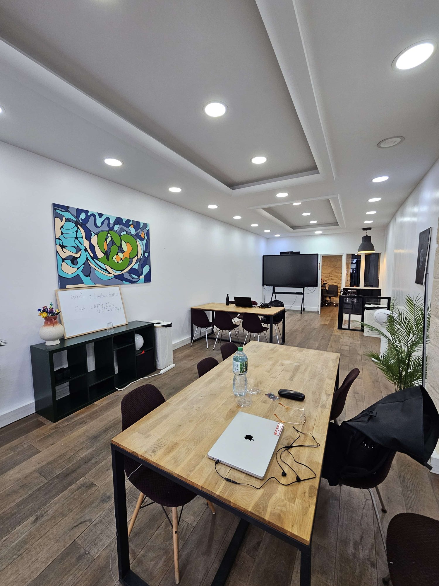 La salle en configuration travail : grandes tables en chêne, chaises design, grand écran tactile et œuvre murale