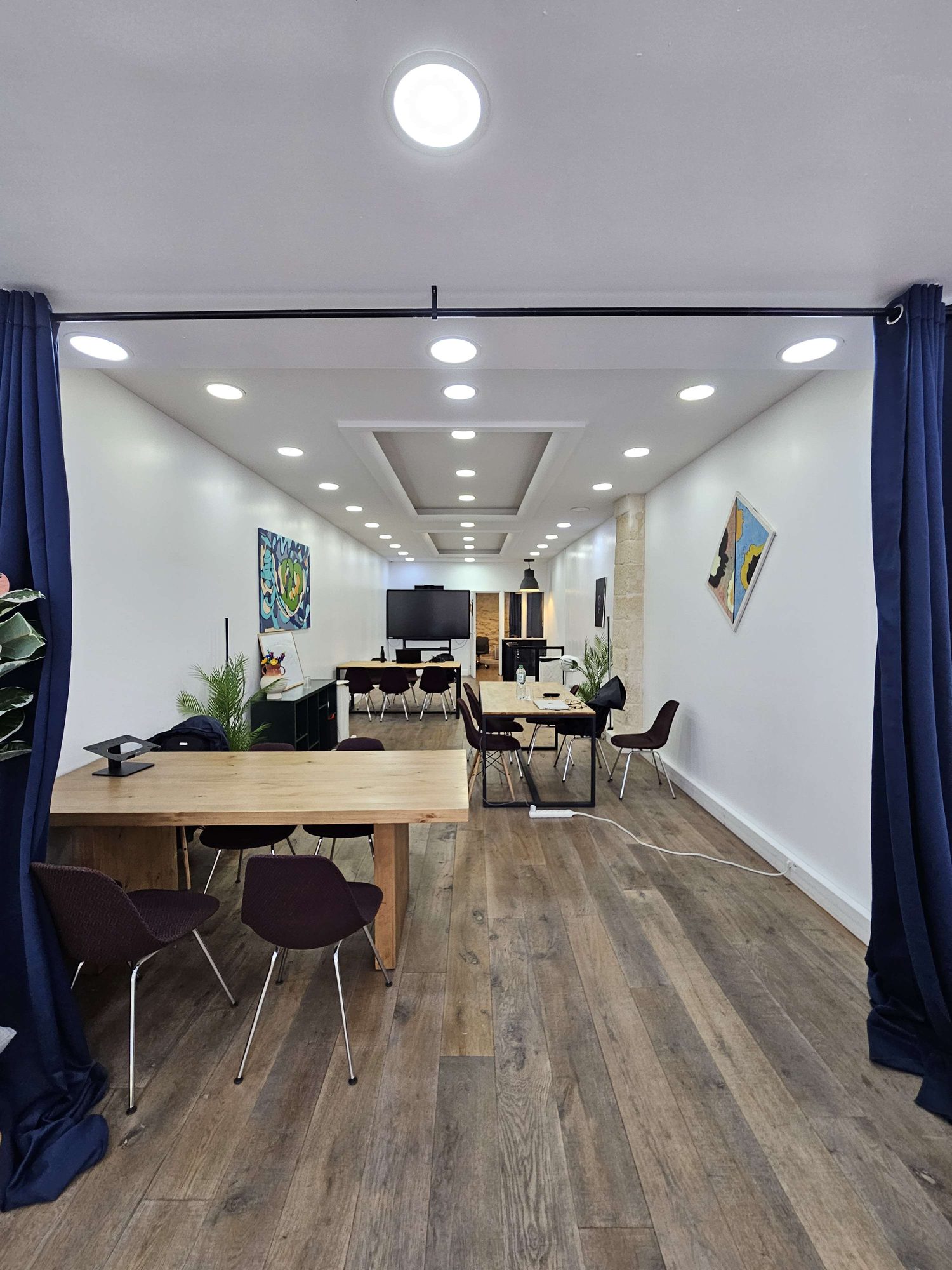 La grande salle swanbase à Paris 2e vue depuis l'entrée : rideaux bleu nuit, parquet en chêne, tables en bois massif, plafonds à caissons lumineux et grand écran au fond